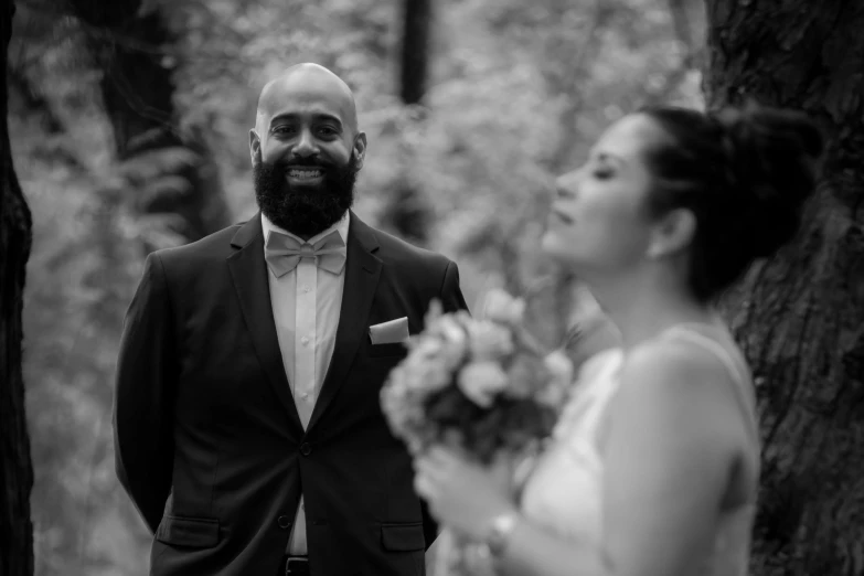 a woman standing next to a man in a suit, a black and white photo, by Jaakko Mattila, pexels contest winner, lush surroundings, with a full black beard, nivanh chanthara, bouquet