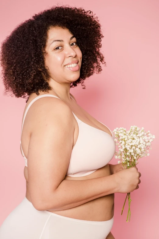 a woman in a white underwear holding a bouquet of flowers, in a black betch bra, pastel pink skin tone, in front of white back drop, looking happy