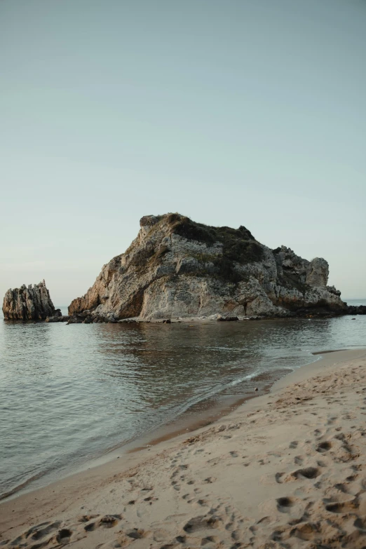 a man standing on top of a sandy beach next to the ocean, piroca, rock arcs, calm evening, greek nose