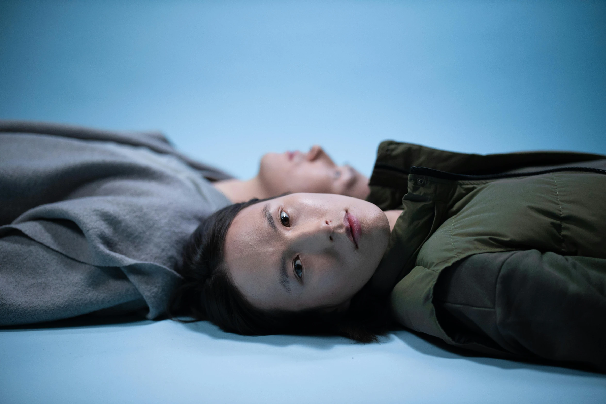 a woman laying on top of a bed next to a man, an album cover, inspired by Zhang Xiaogang, unsplash, hyperrealism, under blue, two young men, movie still 8 k, sangsoo jeong