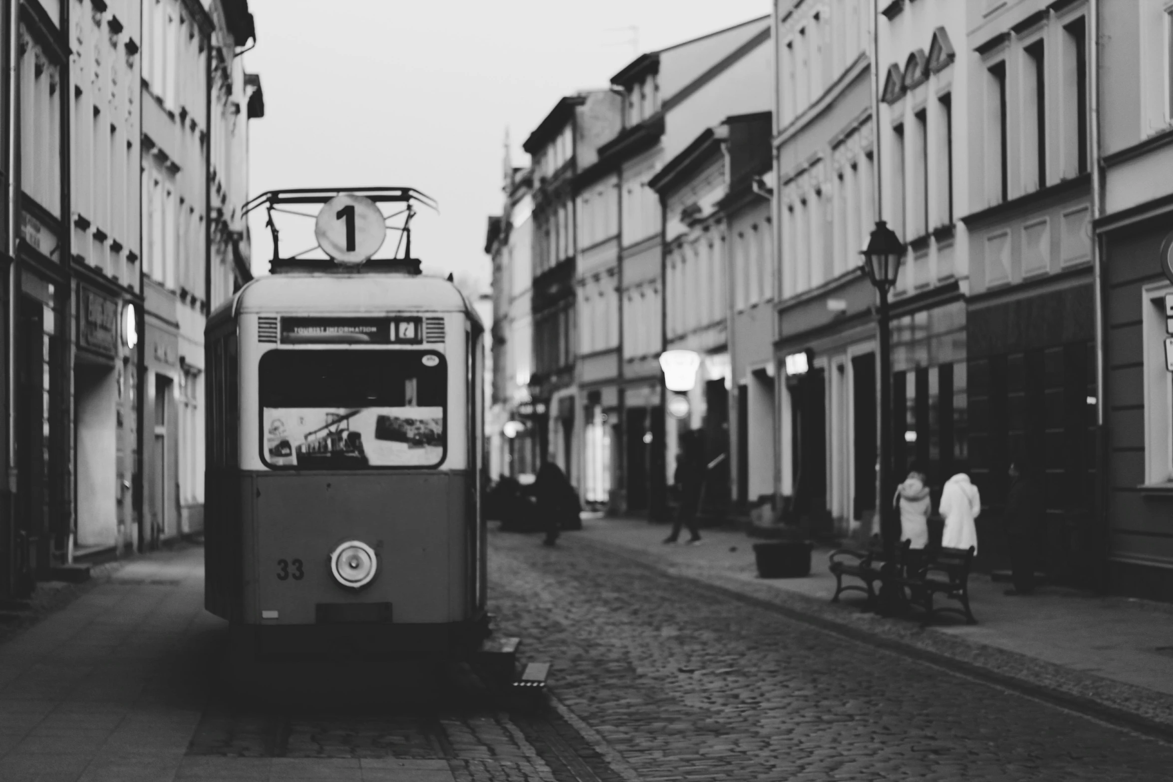 a black and white photo of a trolley on a street, by Adam Marczyński, pexels contest winner, square, town background, train, czeslaw znamierowski