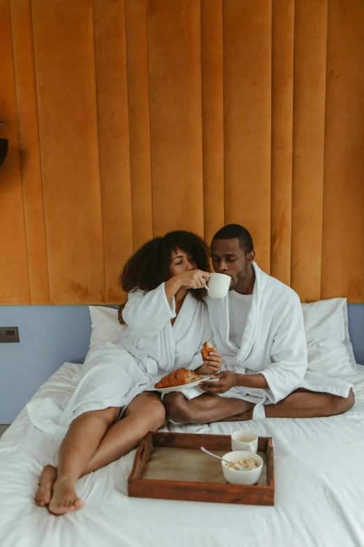 a man and a woman are sitting on a bed, pexels contest winner, having a snack, sleek robes, jamaica, with a white mug