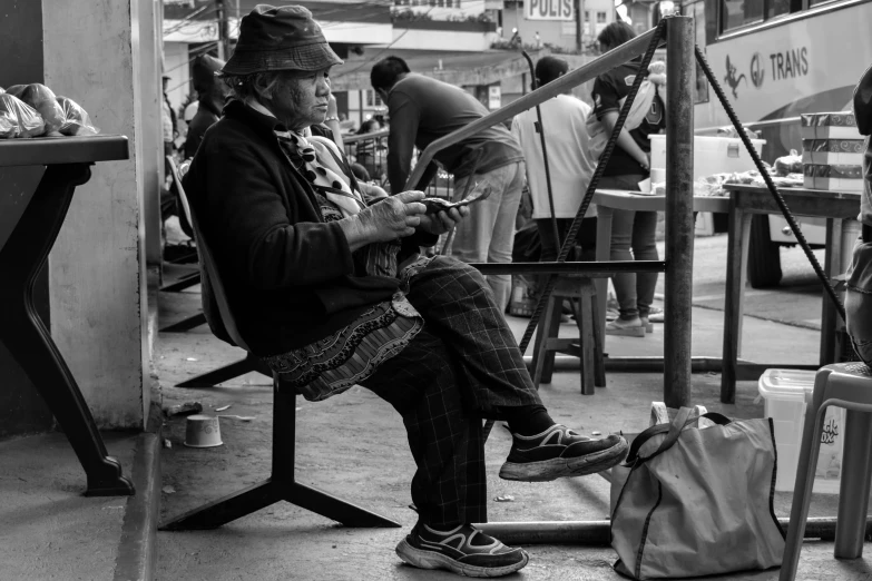 a black and white photo of a man sitting on a bench, process art, street vendors, cellphone, master painter, indigenous man