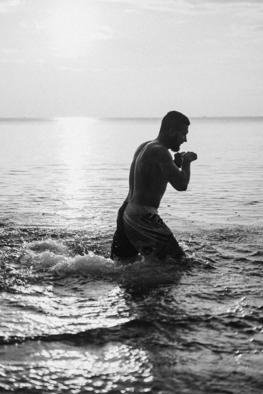 a black and white photo of a man in the water, inspired by Max Dupain, unsplash, happening, boxing stance, sun down, boxer, beach