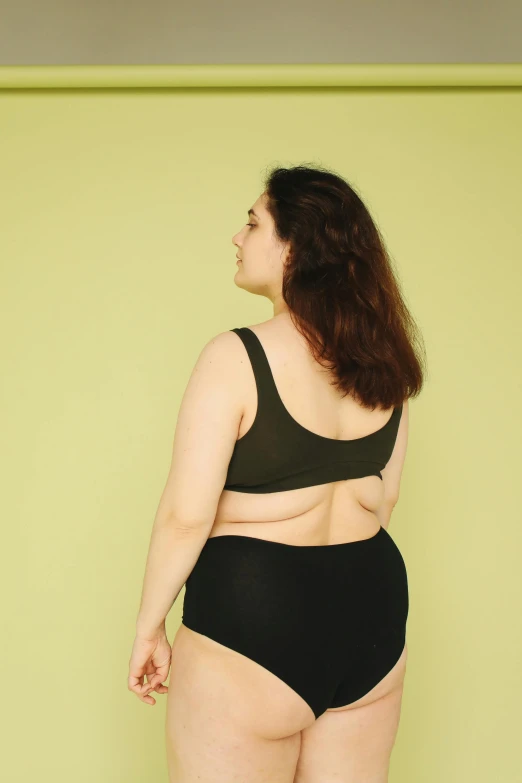 a woman in black underwear standing in front of a green wall, trending on pexels, morbidly obese, facing away, croptop, plain background