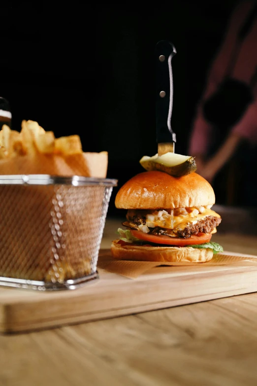 a hamburger sitting on top of a cutting board next to a basket of fries, a picture, lighting, drink, up close, medium angle