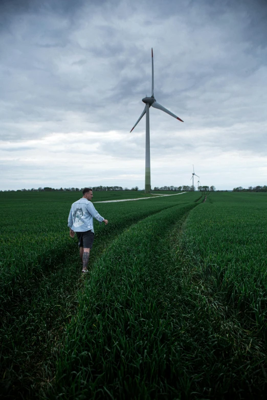 a man standing in a field next to a wind turbine, by Daniel Seghers, happening, trip to legnica, low quality photo, running freely, cinematic shot!