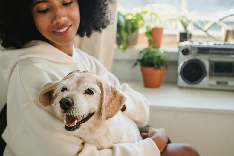 a woman holding a dog in her arms, trending on pexels, wearing a white sweater, at home, thumbnail, digital image