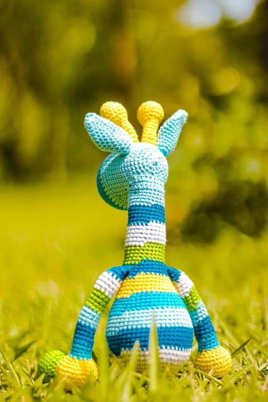 a stuffed giraffe is sitting in the grass, by Paul Bird, yarn, bright colour, sky blue, zoom shot