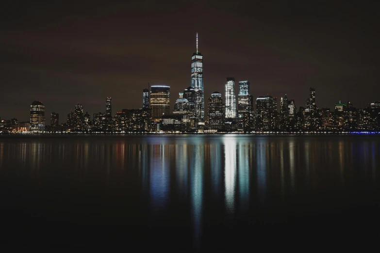 a large body of water with a city in the background, by Sebastian Vrancx, pexels contest winner, new york city at night, background image, reflective lighting, close - up photograph