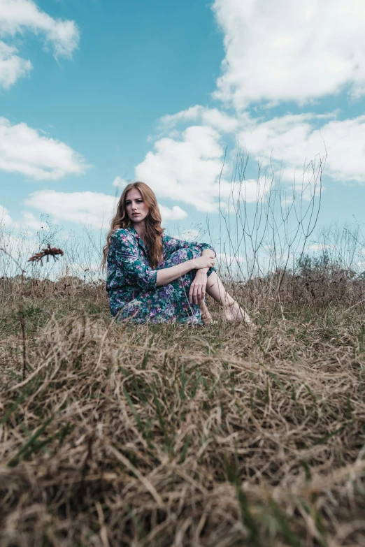 a woman sitting on top of a grass covered field, an album cover, by Will Ellis, ( redhead, looking to the side off camera, standing in midground, blue skies