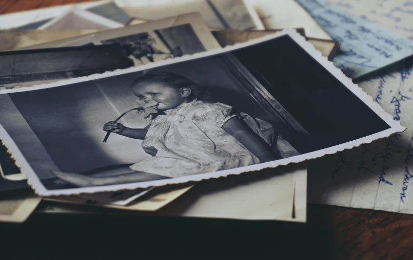 a pile of old photos sitting on top of a table, a black and white photo, by Daniel Lieske, unsplash, photo of the girl, deteriorated, photo from 1940s, vintage colours