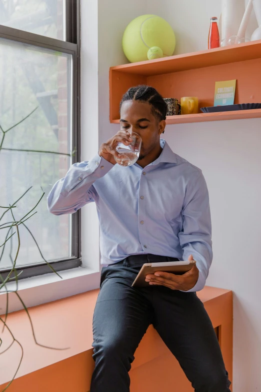 a man sitting on a window sill drinking water, wearing a white button up shirt, using a magical tablet, sitting on a mocha-colored table, water cuastics