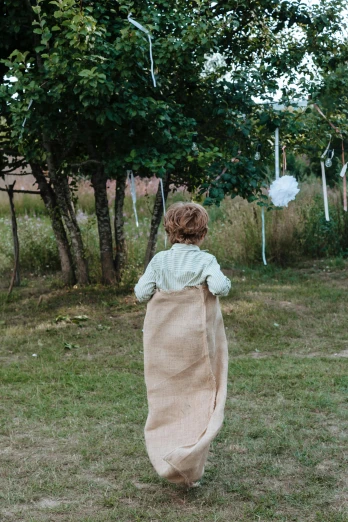 a little girl that is standing in the grass, inspired by Kate Greenaway, unsplash, carrying big sack, decorations, rear-shot, hessian cloth