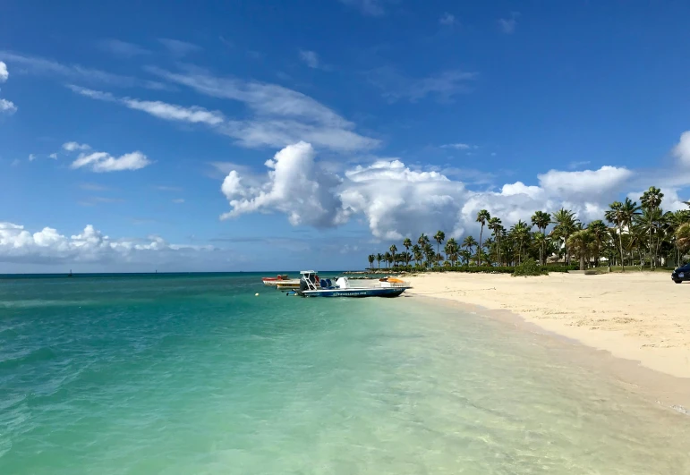 a boat sitting on top of a beach next to the ocean, light blue water