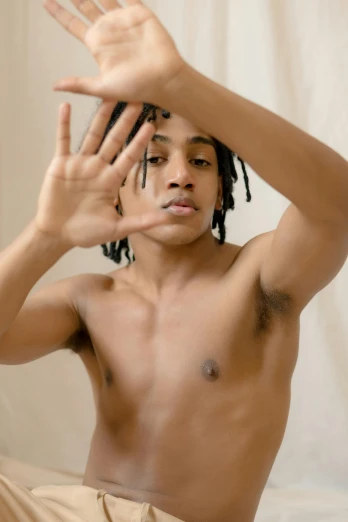 a man with dreadlocks sitting on a bed, an album cover, by Cosmo Alexander, trending on pexels, showing off biceps, nonbinary model, black teenage boy, gestures
