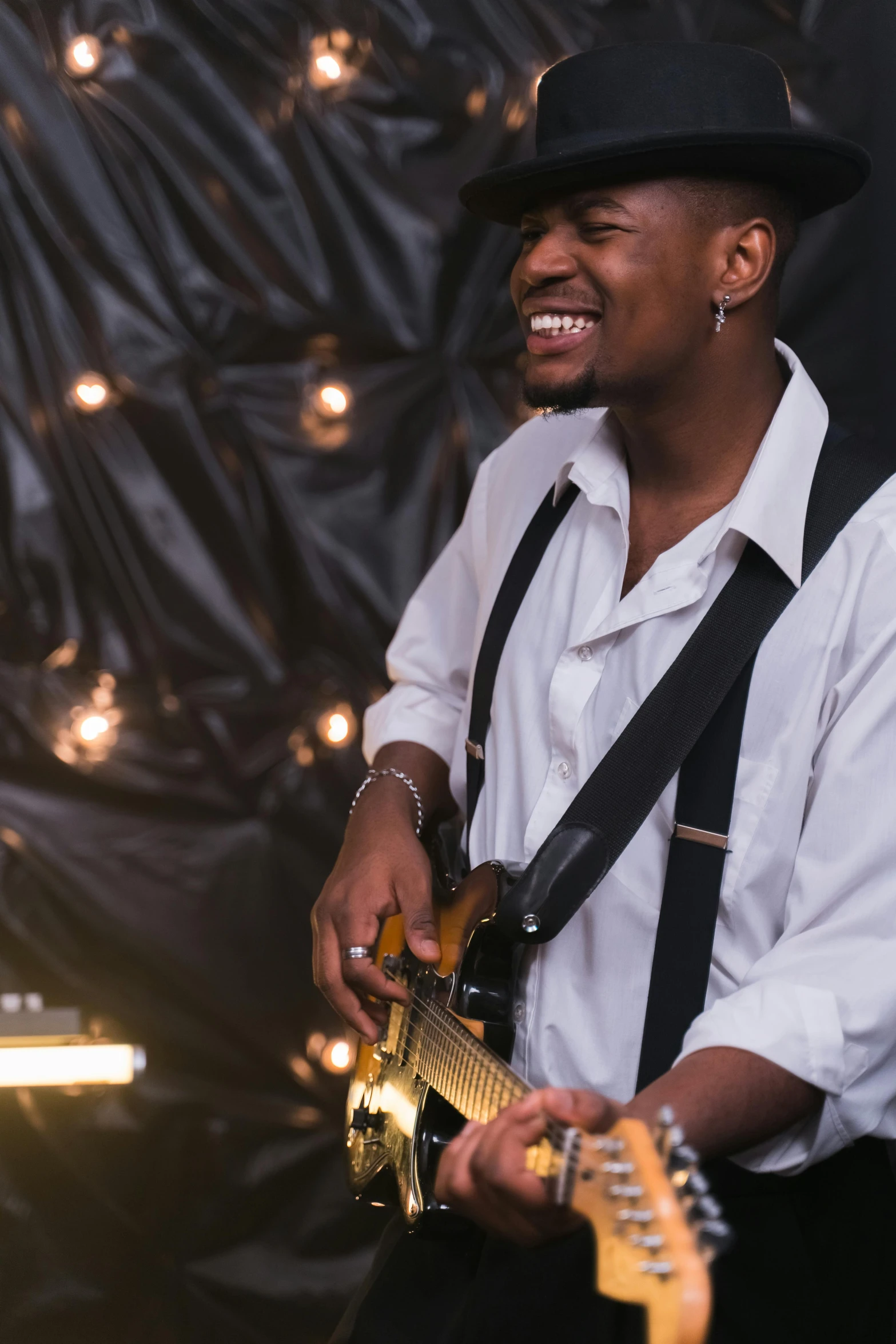 a man in a hat playing a guitar, pexels contest winner, happening, brown skin man with a giant grin, soft lights, over his shoulder, portrait photo of a backdrop