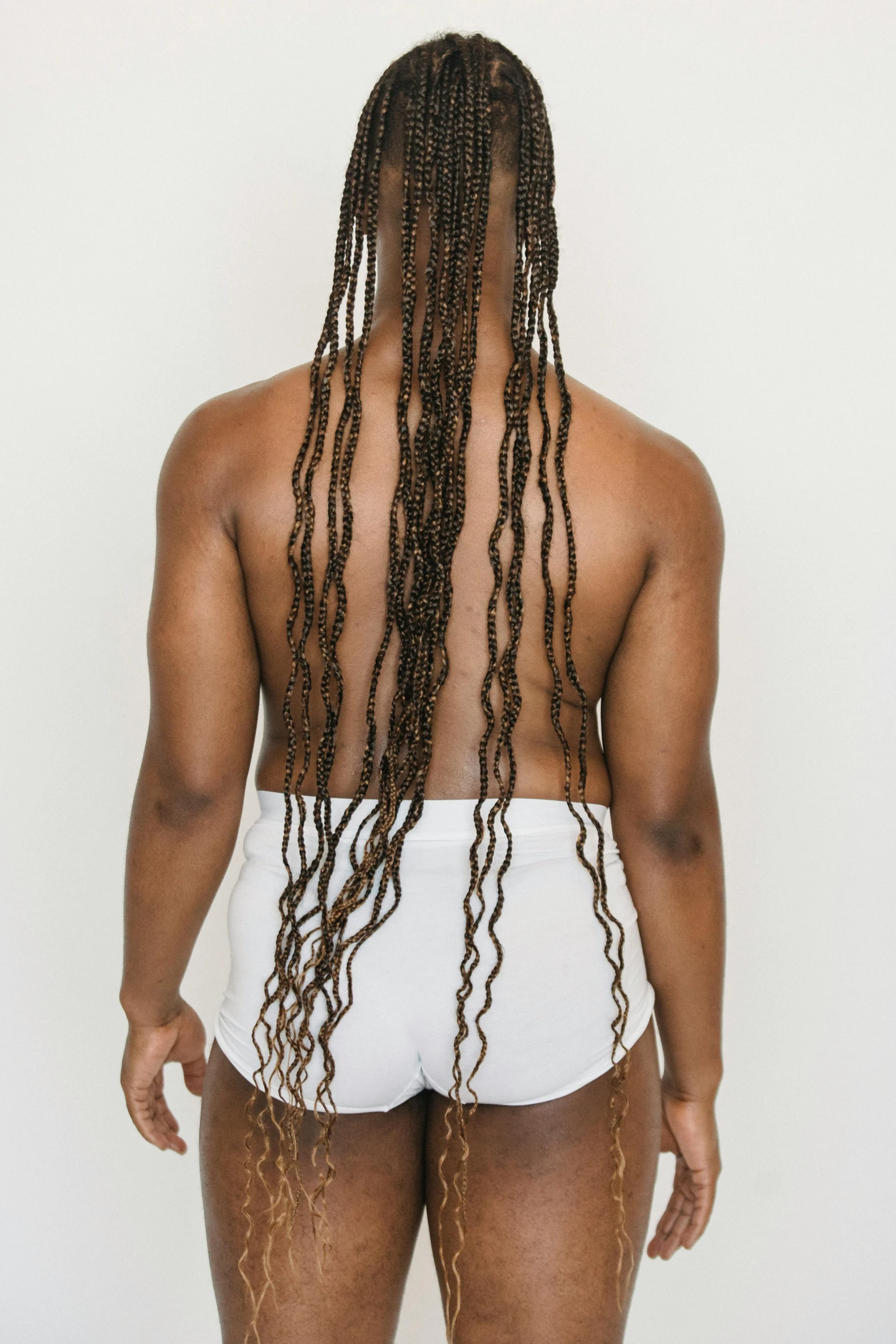 a woman with dreadlocks standing in front of a white wall, shaped derriere, wavy hair spread out, with his back turned, upper body image