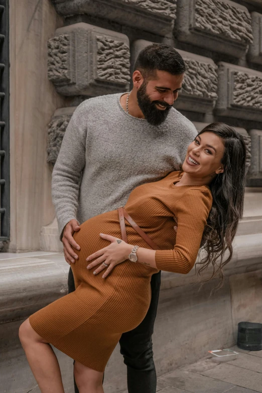 a man and woman standing next to each other in front of a building, pexels contest winner, renaissance, maternity feeling, he is wearing a brown sweater, hispanic, profile image