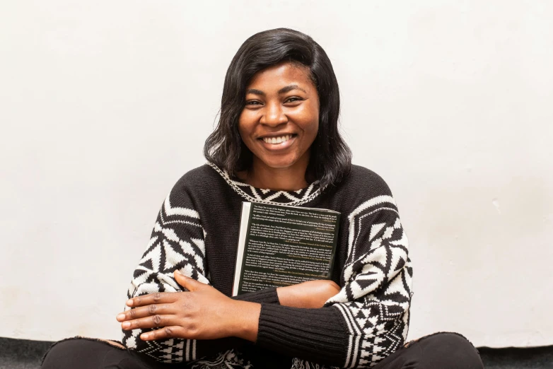 a woman sitting on the floor holding a book, by Ella Guru, hurufiyya, on clear background, while smiling for a photograph, panel of black, holding notebook