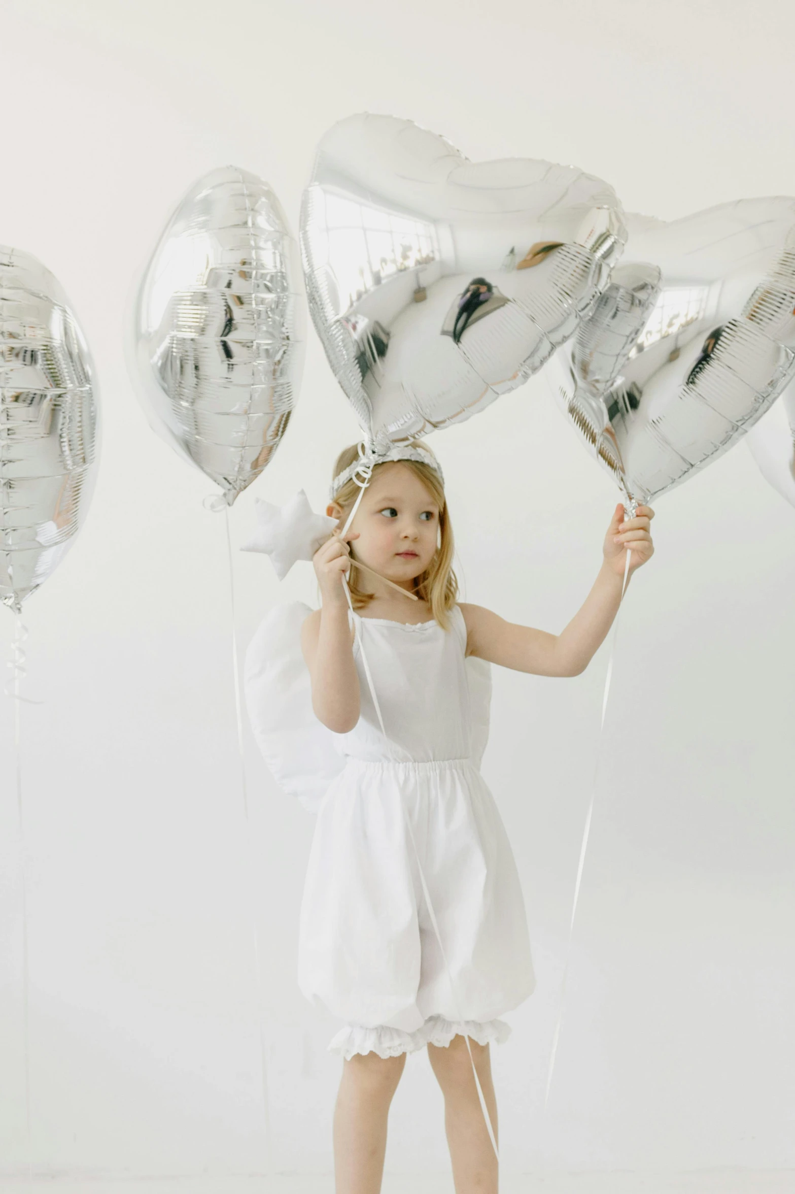 a little girl holding a bunch of heart shaped balloons, inspired by Elsa Beskow, white and silver, chrome outfit, all white, bows