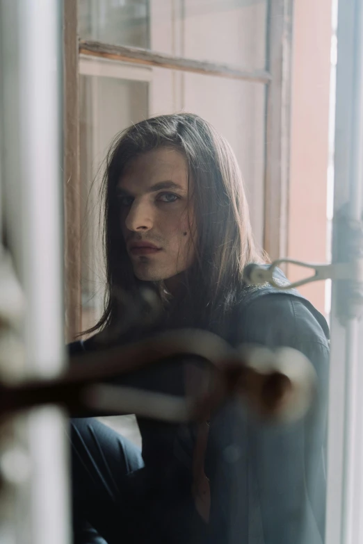 a man with long hair sitting in front of a window, inspired by Elsa Bleda, androgynous face, orelsan, nonbinary model, doors