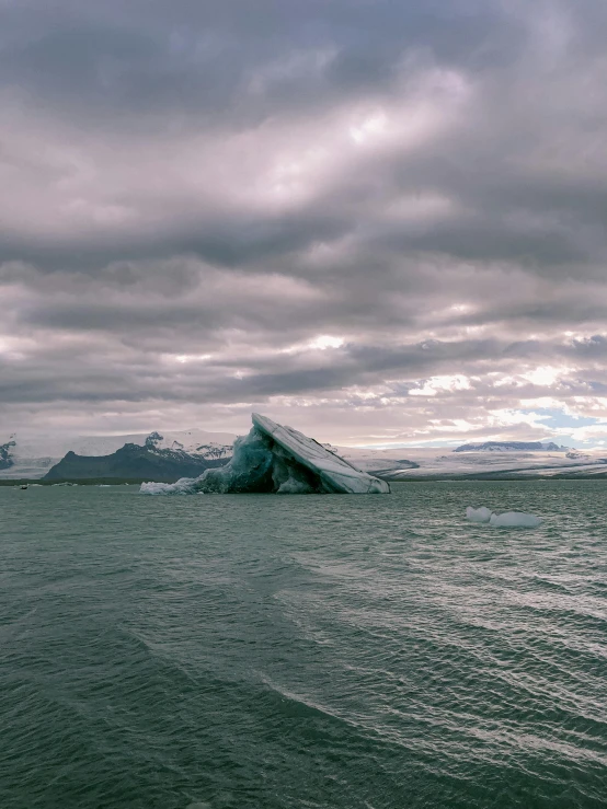 an iceberg in the middle of a body of water, by Sven Erixson, pexels contest winner, dark clouds in the distance, 2022 photograph, 4k), 4 k )