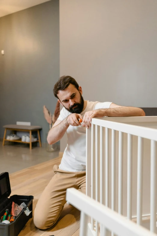 a man sitting on the floor next to a crib, pexels contest winner, modernism, stretching to walls, bearded and built, neuroscience, charging plug in the chest