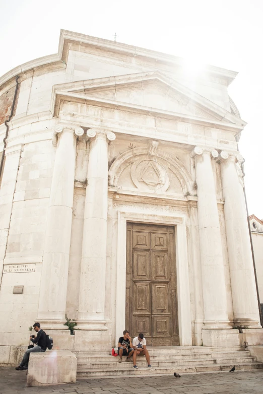 a couple of people that are sitting in front of a building, inspired by Jacopo de' Barbari, trending on unsplash, romanesque, mausoleum, morning sunlight, tall door, white marble buildings