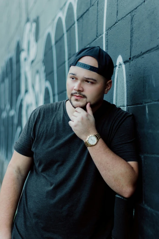 a man leaning against a wall with his hand on his chin, a portrait, inspired by Eddie Mendoza, unsplash, post malone, he is wearing a black t-shirt, jontron, watch photo