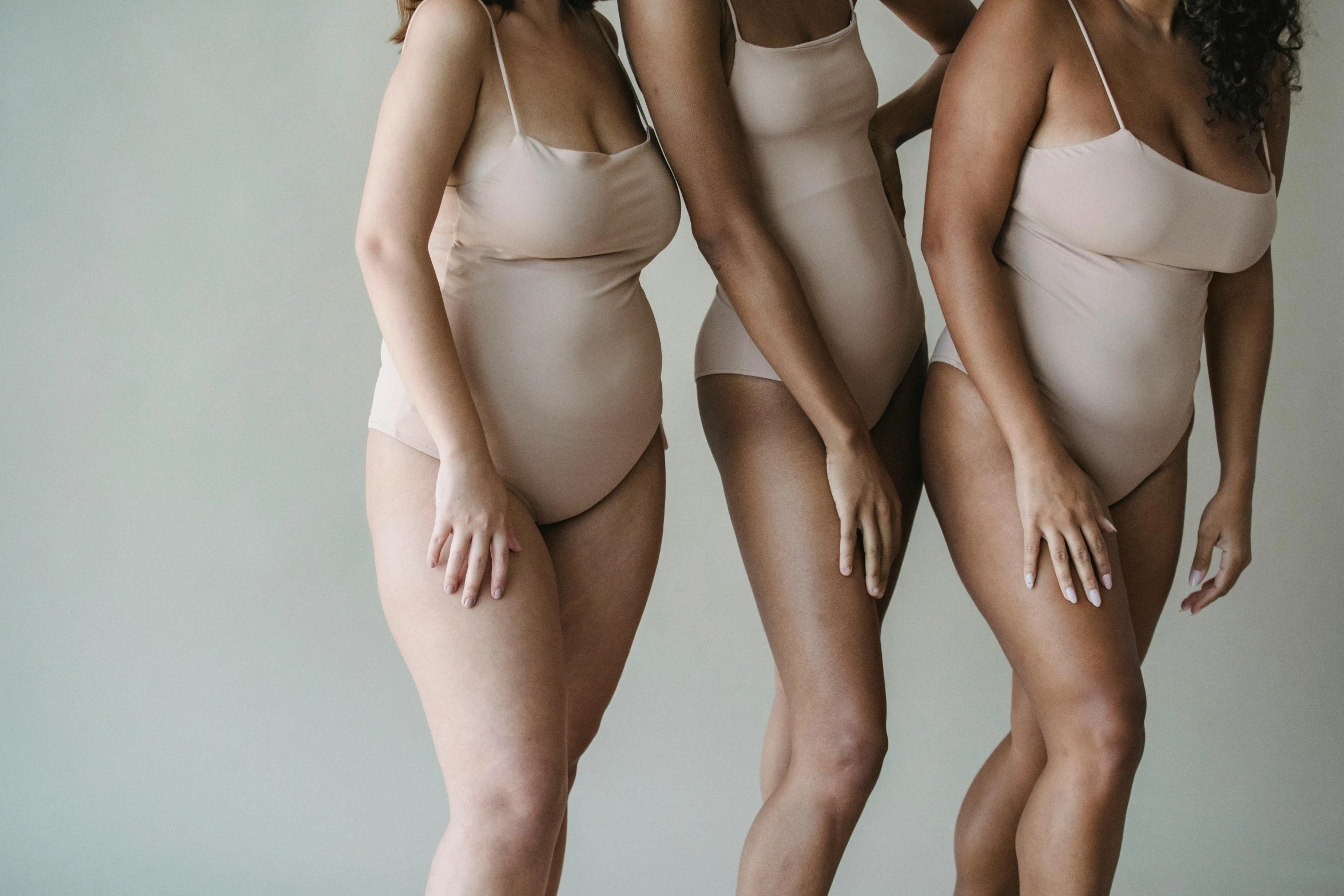 a group of three women standing next to each other, inspired by Vanessa Beecroft, trending on pexels, renaissance, round thighs, beige cream natural muted tones, is wearing a swimsuit, slightly overweight