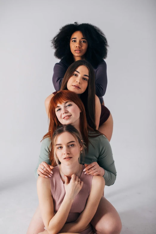 a group of women sitting on top of each other, one is a redhead, light skin tone, on top of it, body and headshot