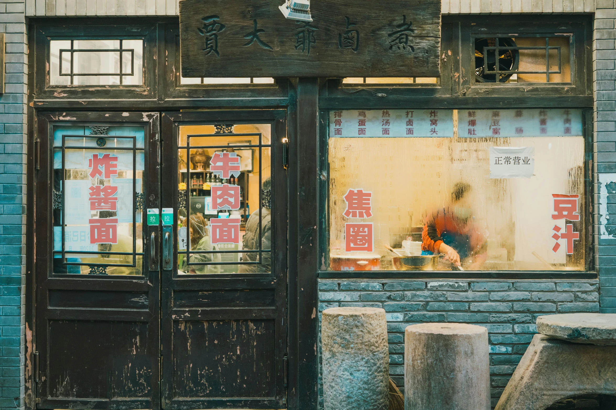 a man sitting at a table in front of a restaurant, a silk screen, inspired by Zhang Kechun, pexels contest winner, mingei, shop front, buildings carved out of stone, pan ren wei, an escape room in a small