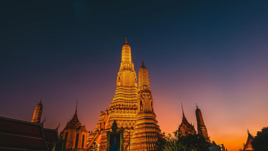 a very tall building sitting in the middle of a city, glowing temple in the distance, thai architecture, warm glow from the lights, thumbnail