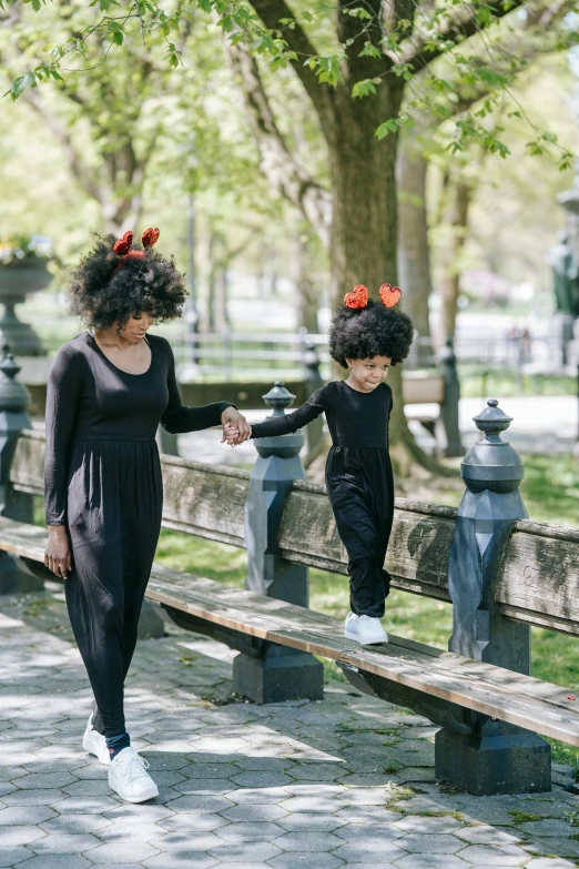 a woman walking next to a child on a park bench, by Lily Delissa Joseph, long black crown, black curly hair, costume, black