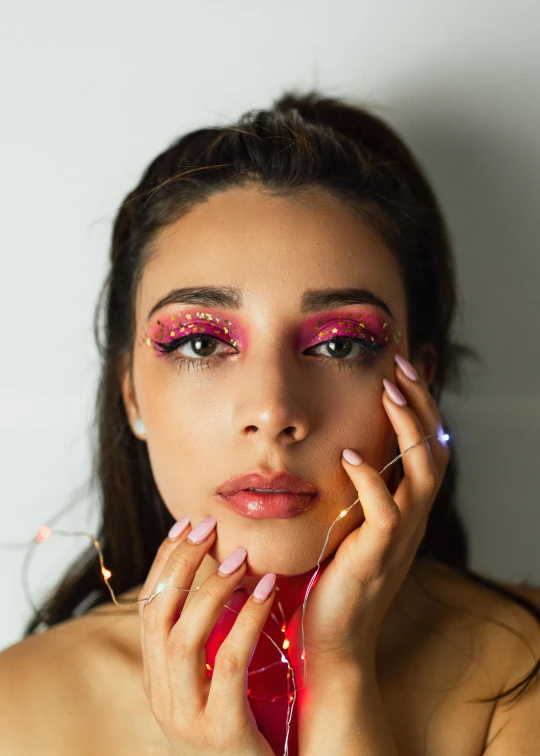 a woman with pink makeup posing for a picture, an album cover, trending on pexels, glitter accents on figure, red contacts, hands on face, high quality photo