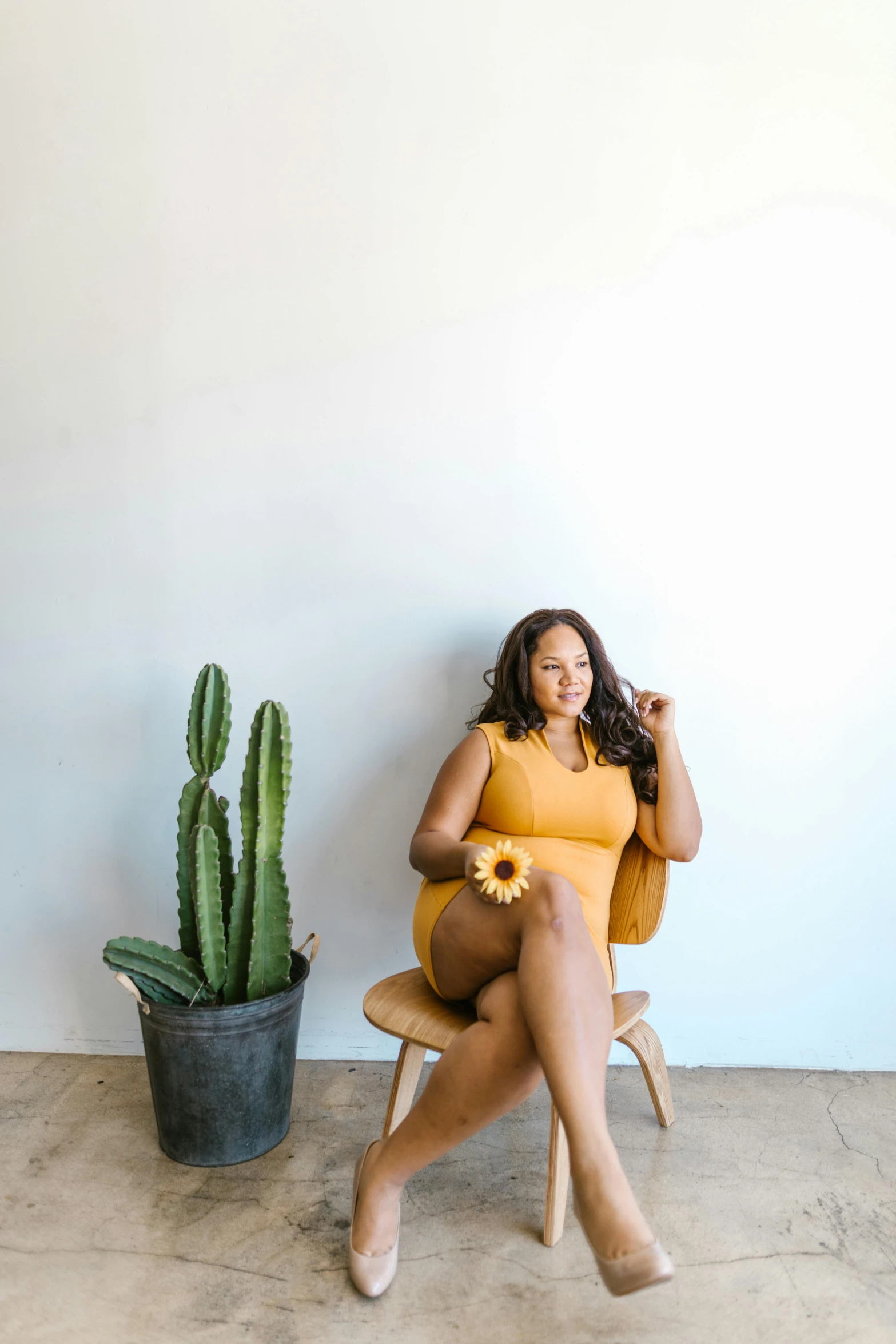 a woman sitting in a chair next to a cactus, a portrait, by Dulah Marie Evans, trending on unsplash, plus size, colors : yellow sunflowers, round thighs, studio shot