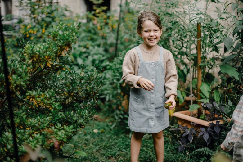 a little girl that is standing in the grass, wearing an apron, moonlight grey, with two front pockets, foliage clothing