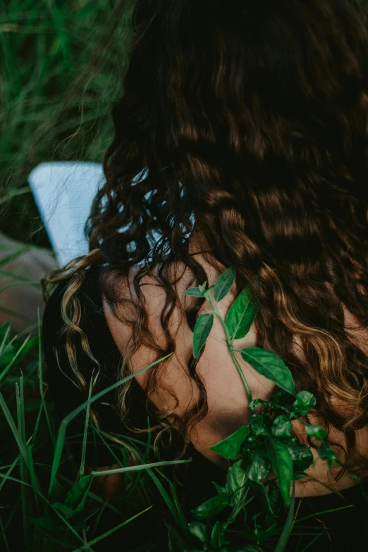 a woman sitting in the grass with her back to the camera, inspired by Elsa Bleda, trending on pexels, renaissance, with curls, greenery, ignant, close - up photograph