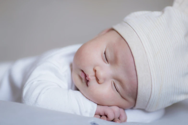 a close up of a baby sleeping on a bed, white cap, bao pham, relaxed pose, right hand side profile