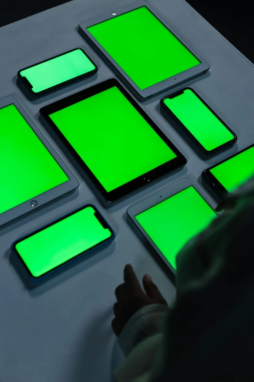 a group of cell phones sitting on top of a table, a hologram, interactive art, monochromatic green, using a magical tablet, colored gel lighting, green crt monitors