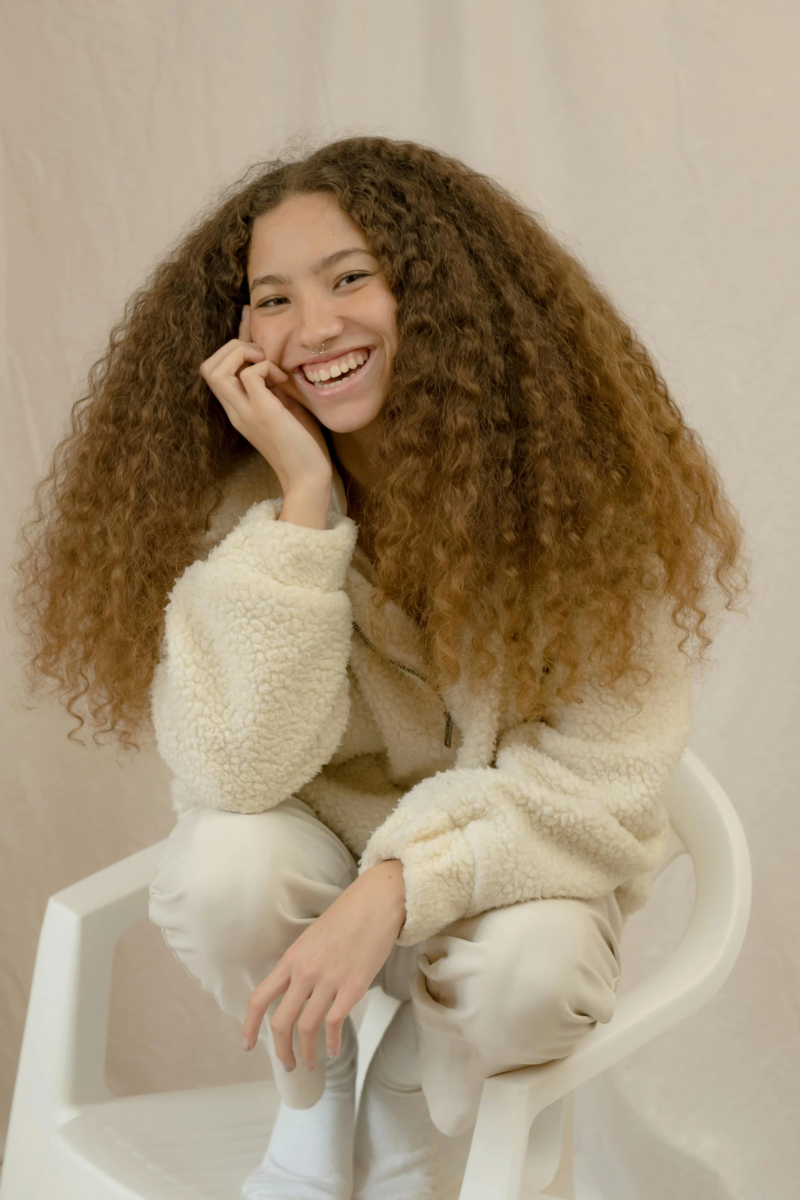 a woman sitting on top of a white chair, trending on pexels, renaissance, long brown puffy curly hair, wearing a sweater, wearing a track suit, fluffy full of light