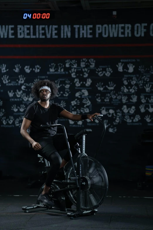 a man that is sitting on a bike, in a black room, with afro, in a gym, lachlan bailey