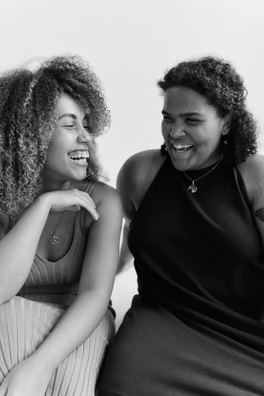 a couple of women sitting next to each other, a black and white photo, by Carey Morris, pexels, lizzo, dark short curly hair smiling, bowater charlie and brom gerald, white and black clothing