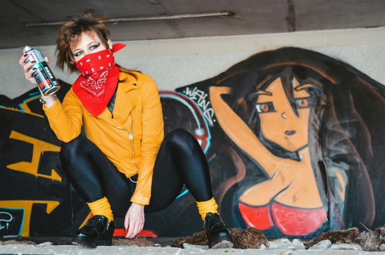 a woman sitting in front of a graffiti covered wall, unsplash contest winner, red bandana, yellow clothes, wearing bandit mask, photo of young woman