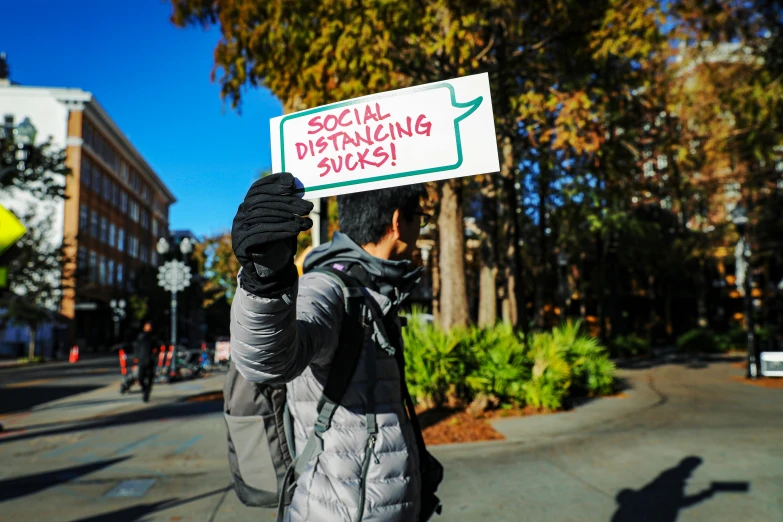 a person holding a sign that says social distancing sucks, a photo, by Julia Pishtar, shutterstock, sots art, san francisco, square, college, walk