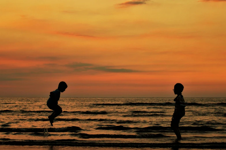 a couple of people standing on top of a beach, by Jan Tengnagel, pexels contest winner, kids playing, leaping, calm evening, cardboard