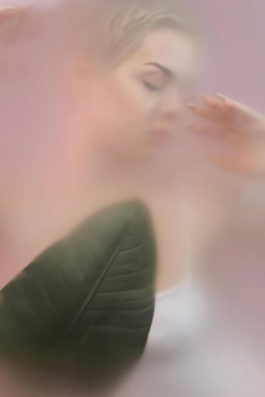 a woman holding a green leaf in front of her face, a picture, by Anna Füssli, aestheticism, pink mist, soft motion blur, promo image, bathing in light