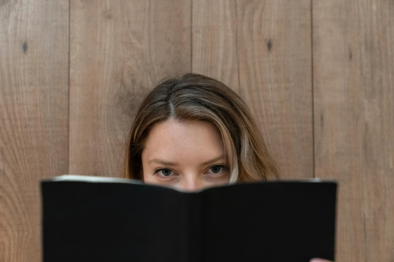 a woman reading a book in front of a wooden wall, pexels contest winner, third eyes middle of foreheads, black, pareidolia, slightly minimal