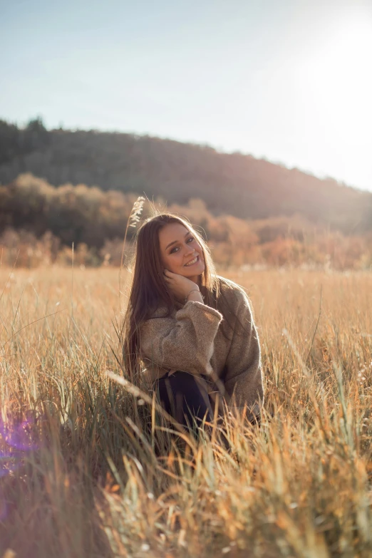 a woman sitting in a field of tall grass, a picture, by Marshall Arisman, unsplash, wearing an oversized sweater, elegant smiling pose, instagram post, in fall